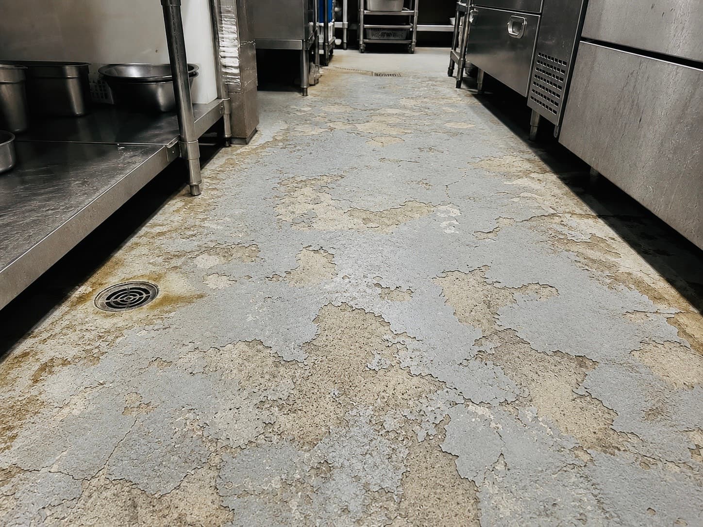 業務用厨房の通路で塗膜が剥がれ床材が露出している状態（施工前）