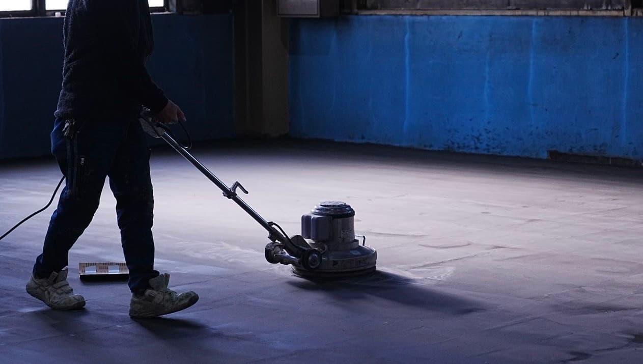 代表の神山氏が施工完了後の光沢のある床(工場背景)でカメラを直視